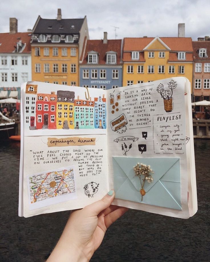 someone is holding up an open book with pictures and words on it in front of some buildings