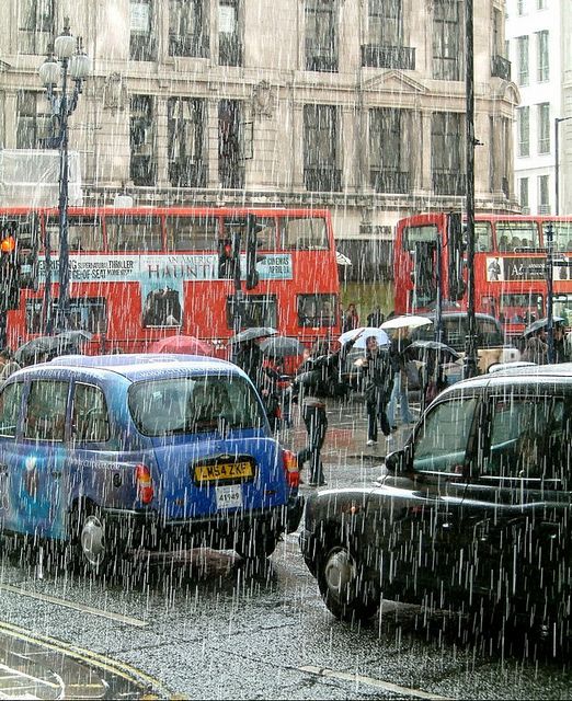 people walking in the rain with umbrellas and cars on a city street near double decker buses