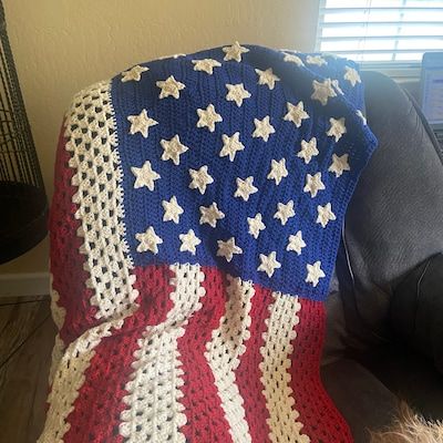 an american flag crocheted afghan is draped over a black leather chair in front of a window