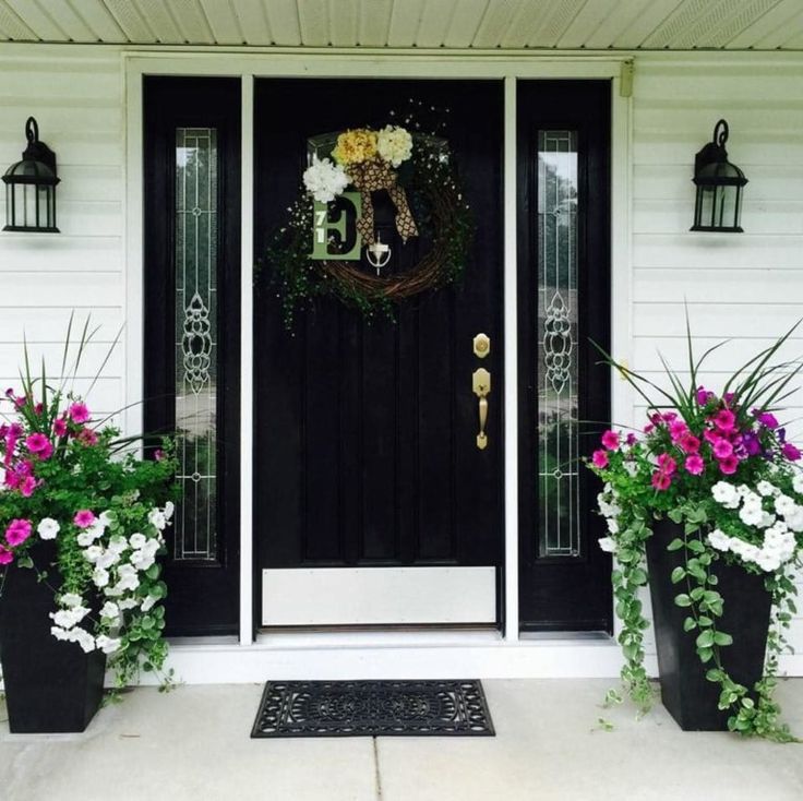 two planters with flowers are next to the front door that has a wreath on it