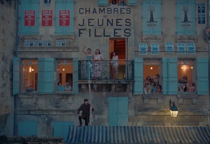 people are standing on the balcony of an old building with shutters and windows in front of them