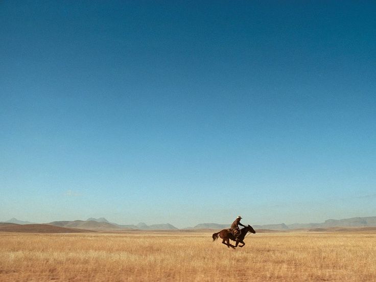 a man riding a horse across a dry grass field