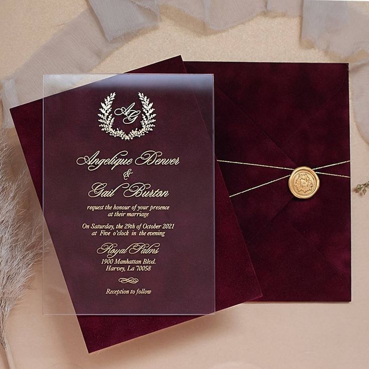 a wedding card with a wax seal on it next to an envelope and some feathers