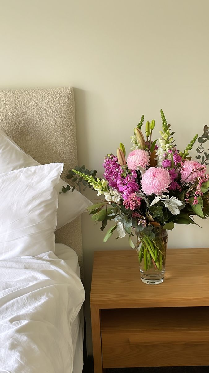 a vase filled with pink and white flowers sitting on top of a table next to a bed