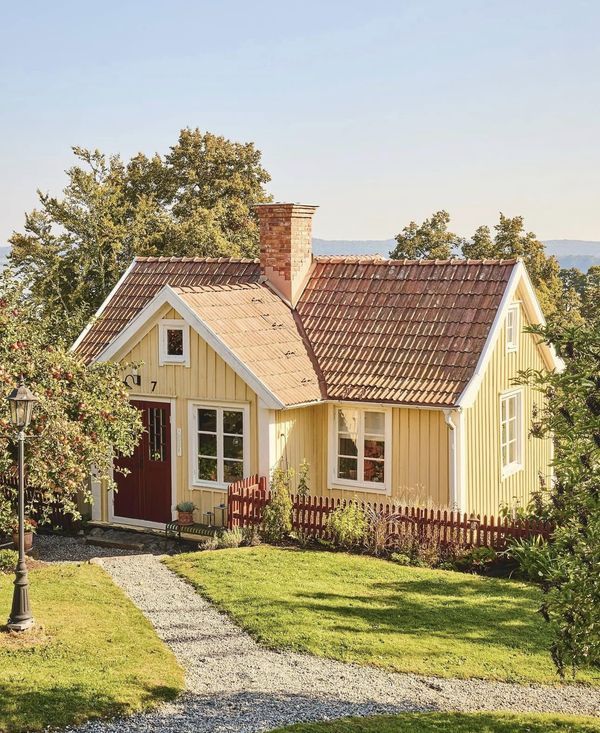 a small yellow house with a red door and brown shingles on the top floor