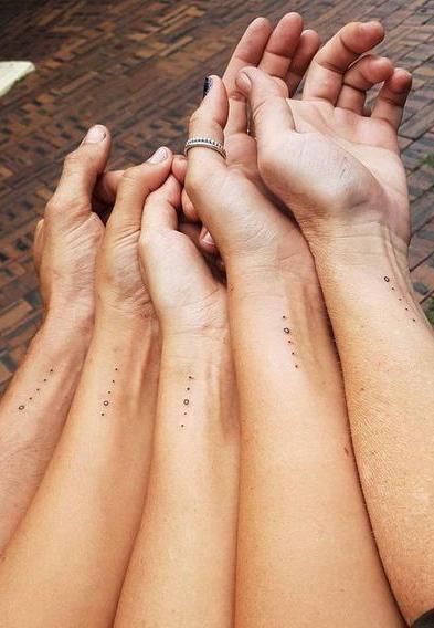 four people are holding their hands together with small dots on the wrist and hand tattoos