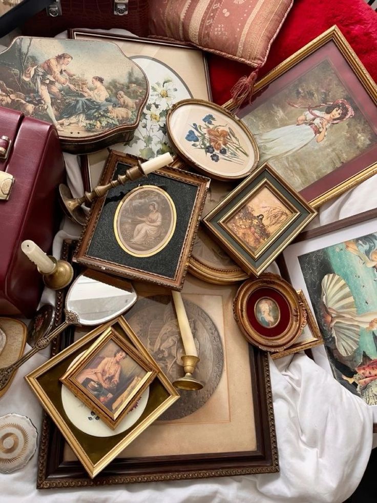 an assortment of framed and unframeed art on a bed with a red pillow