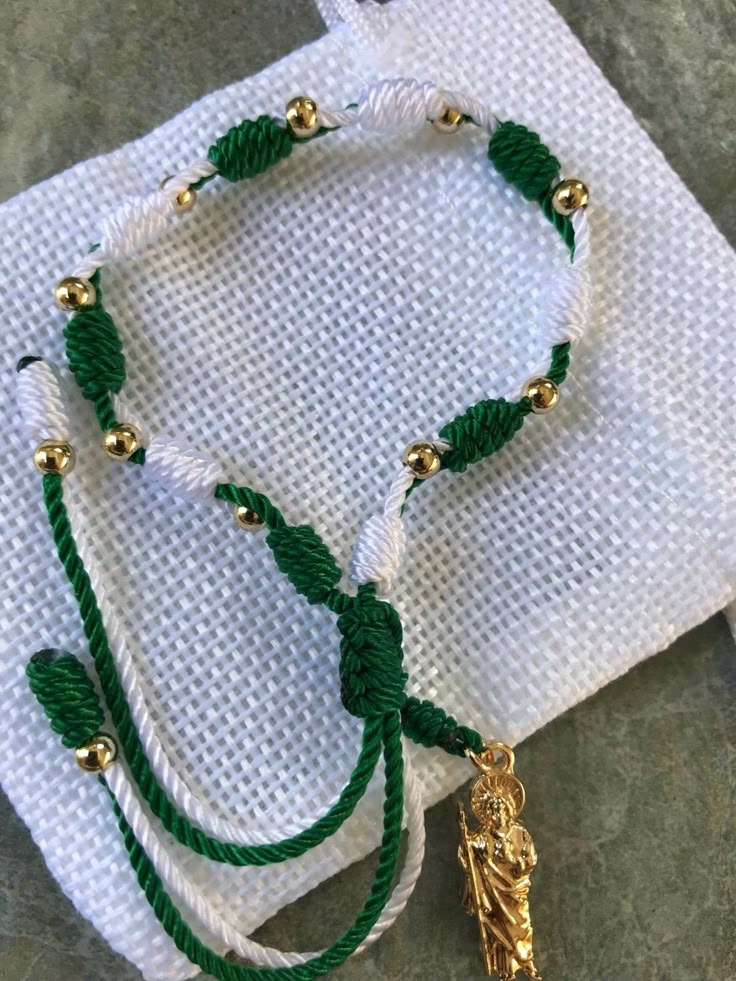 "Handmade, adjustable green and white st. Judas Thaddeus plated gold beads bracelet. Material: nylon string/green and white #18, #9 plated gold 14k beads 4mm St. Judas Thaddeus plated gold pendant 2.50cm Bracelet made for unisex adults,minimum slide lock from 7\" inches to 8.5\" inches ; perfect for a gift!" Adjustable Green Bracelets With Gold Beads, San Judas Bracelet, Handmade Adjustable Green Rosary Bracelet, Green Handmade Adjustable Rosary Bracelet, Adjustable Handmade Green Rosary Bracelet, Mexican Bracelet Ideas, Mexican Beaded Jewelry, Mexican Bracelets Handmade, Bracelets From Mexico