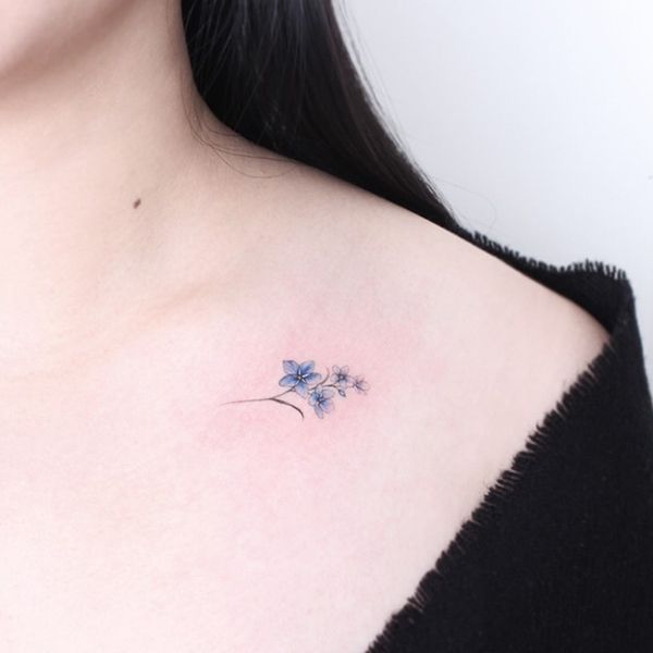 a woman's chest with a small blue flower tattoo on the left side of her neck