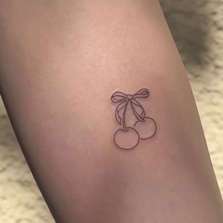 a small cherry tattoo on the left side of the leg, with a bow at the top