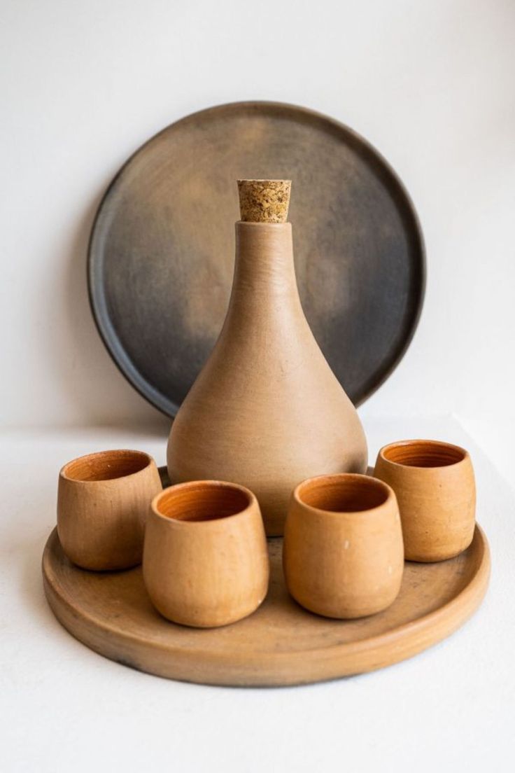 a set of four wooden cups and a vase on a tray with a plate in the background