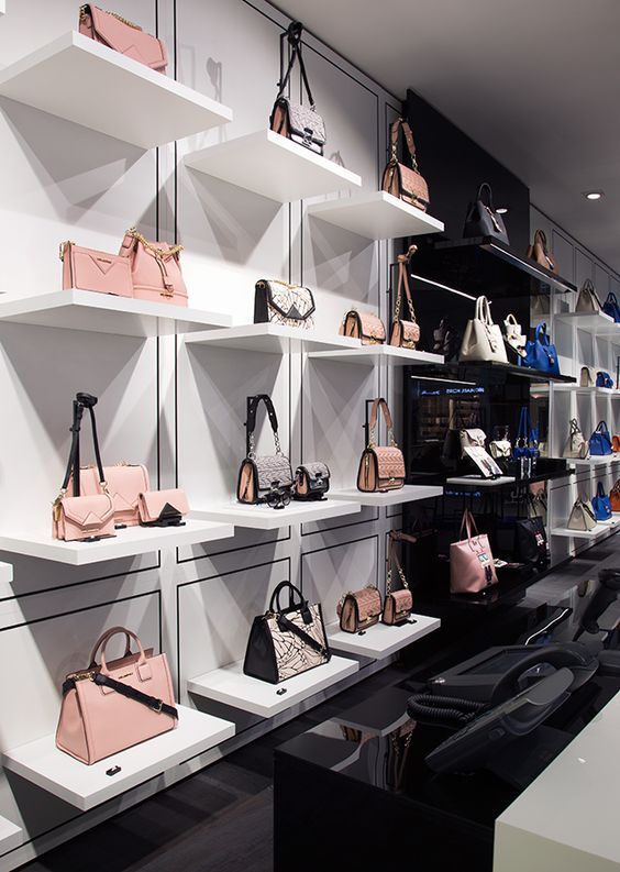 a display case filled with lots of purses and handbags on white shelving