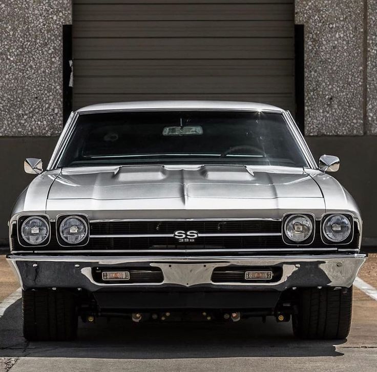 the front end of a silver muscle car parked in a parking lot next to a garage door