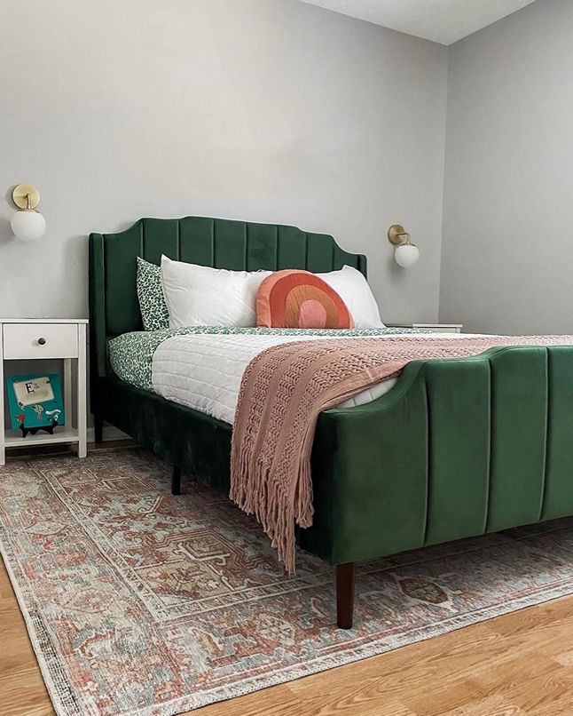 a green bed sitting on top of a wooden floor next to a white dresser and lamp