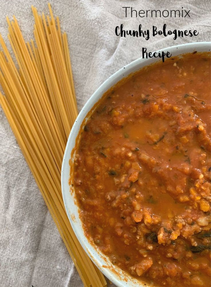 there is a bowl of chili and noodles on the table next to some chopsticks