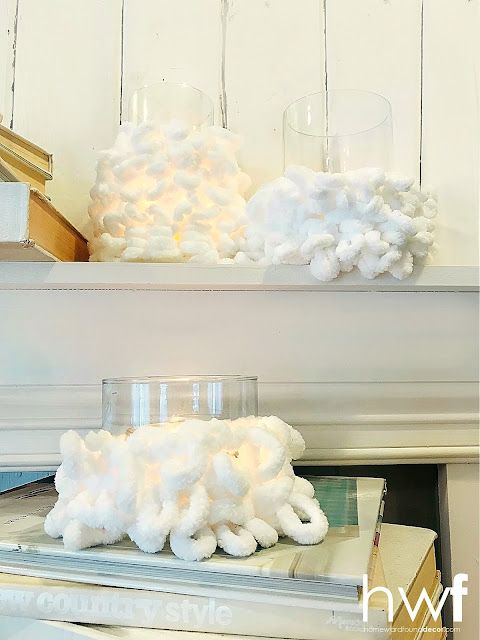 two white candles sitting on top of a shelf next to books and glass vases