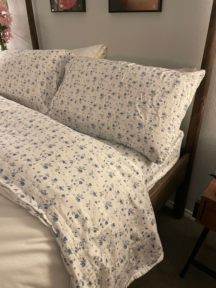 a bed with white sheets and blue flowers on the comforter is next to two framed pictures