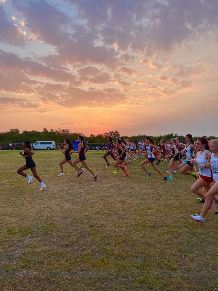 a group of people running across a grass covered field under a pink and blue sky