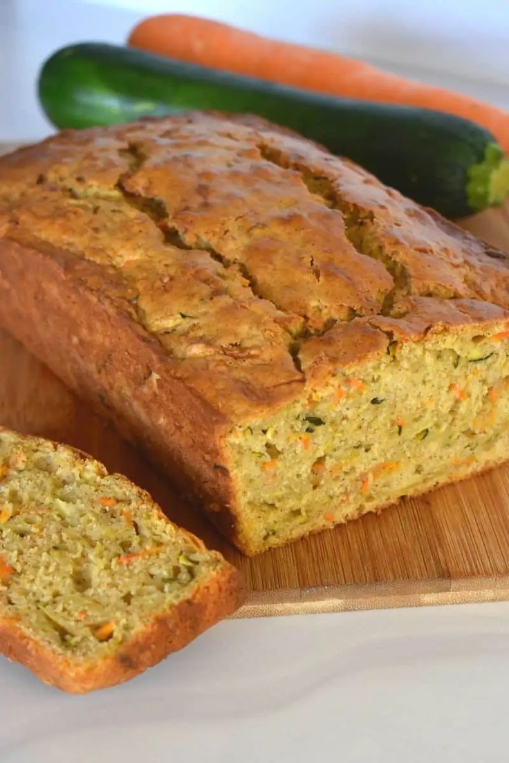 a loaf of zucchini bread sitting on top of a wooden cutting board next to carrots