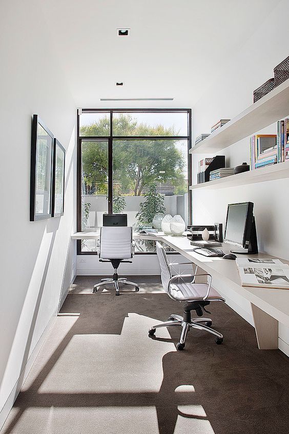 an office area with desks, chairs and bookshelves on the wall in front of large windows