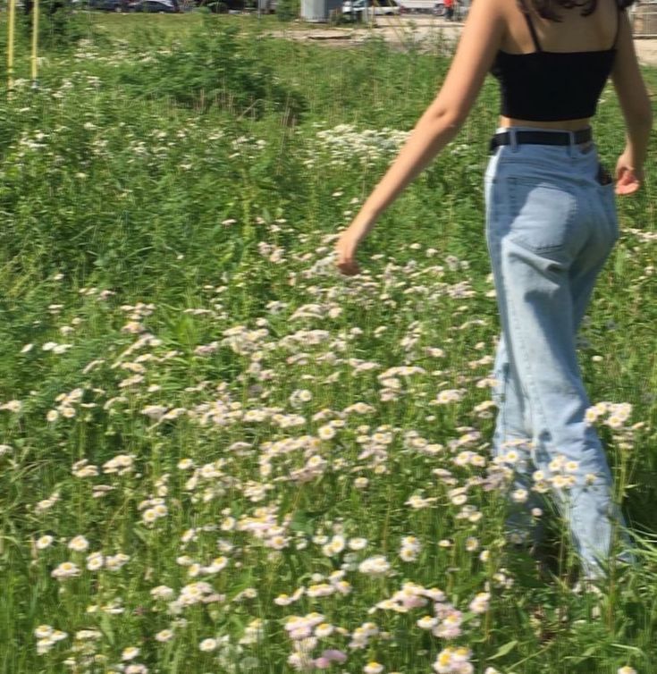 a woman standing in the middle of a field with wildflowers and buildings behind her