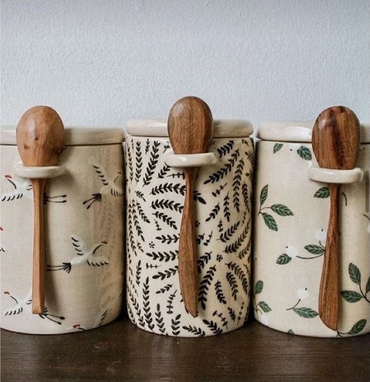 four wooden spoons are lined up next to each other in ceramic containers with designs on them