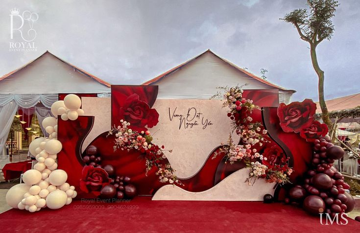 a red and white wedding backdrop with roses, balloons and flowers on the front wall