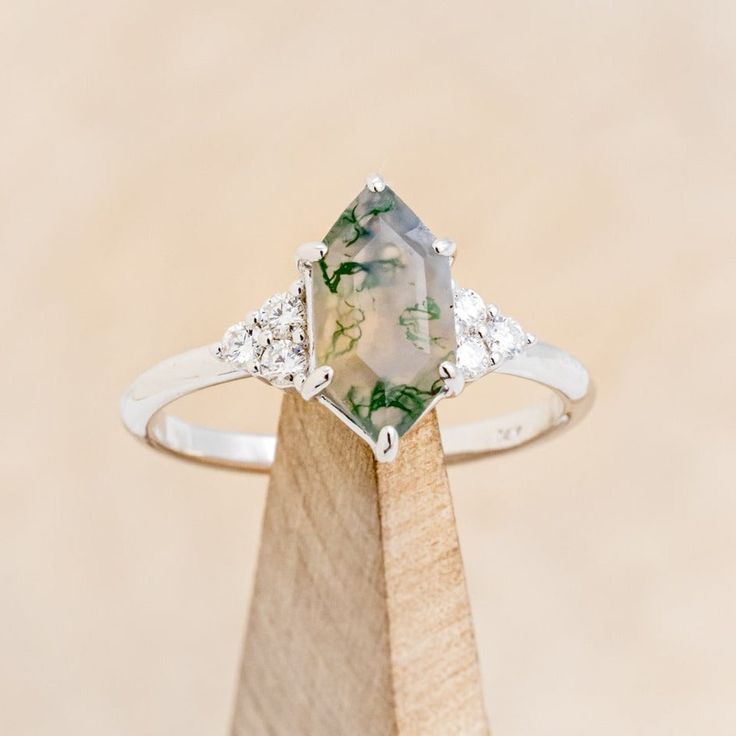 an engagement ring with a green and white stone surrounded by three diamonds on a wooden stand