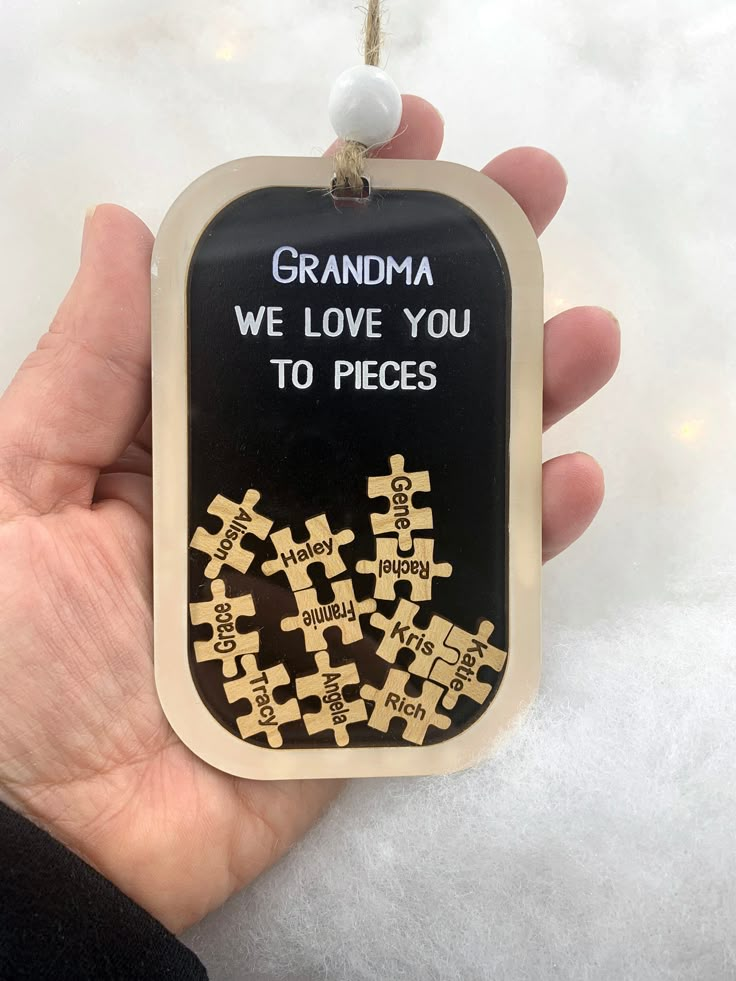 a hand holding a black and gold keychain that says grandma we love you to pieces