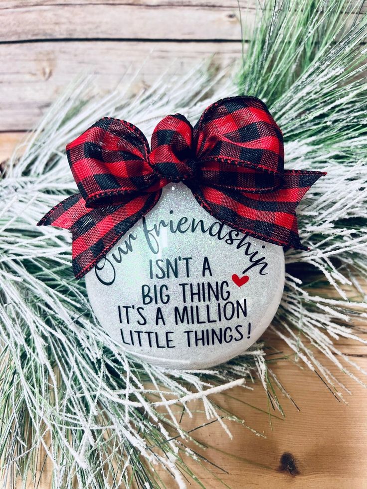 a christmas ornament hanging from a pine tree with red and black plaid ribbon