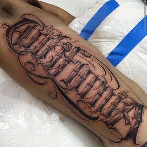 a man laying on top of a bed with a tattoo on his leg and name written in cursive font