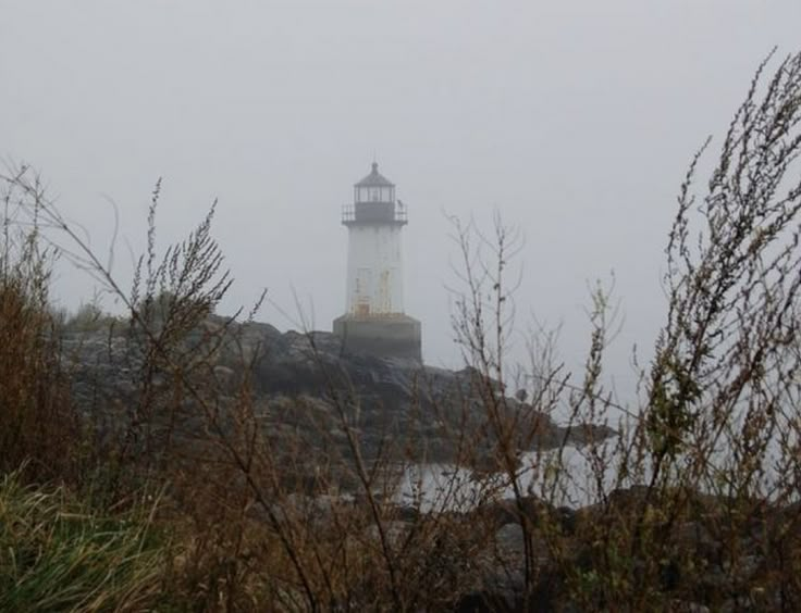 a light house sitting on top of a rocky hill next to the ocean in the fog