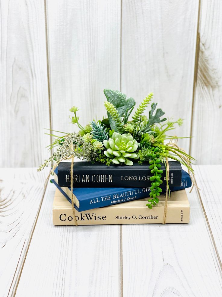 three books stacked on top of each other with succulents and plants in them