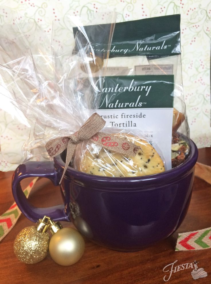 a purple coffee mug filled with cookies and other holiday treats next to a christmas ornament