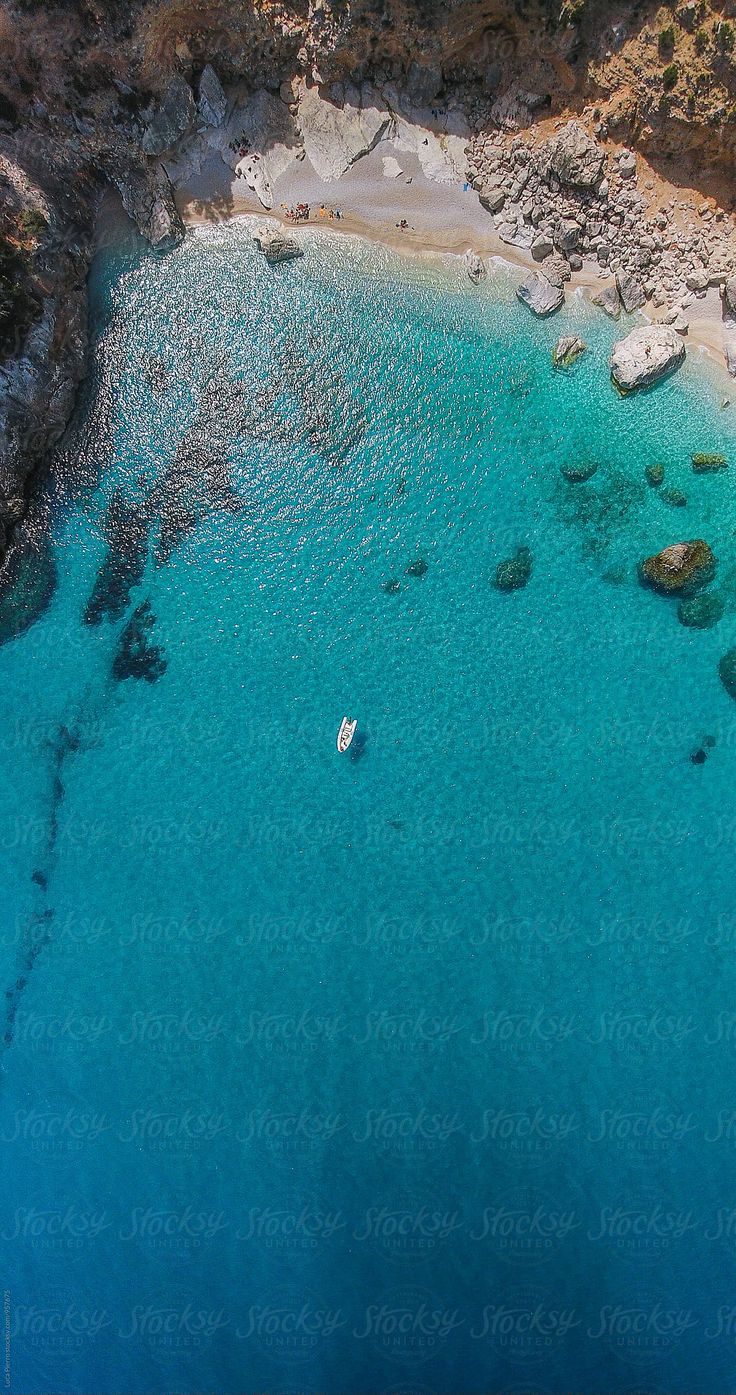 an aerial view of a boat in the water near some rocks and sand on the beach