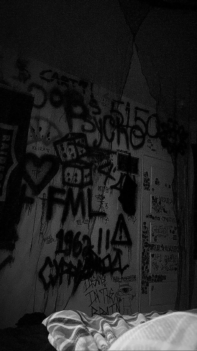 black and white photograph of an unmade bed in a dark room with graffiti on the walls