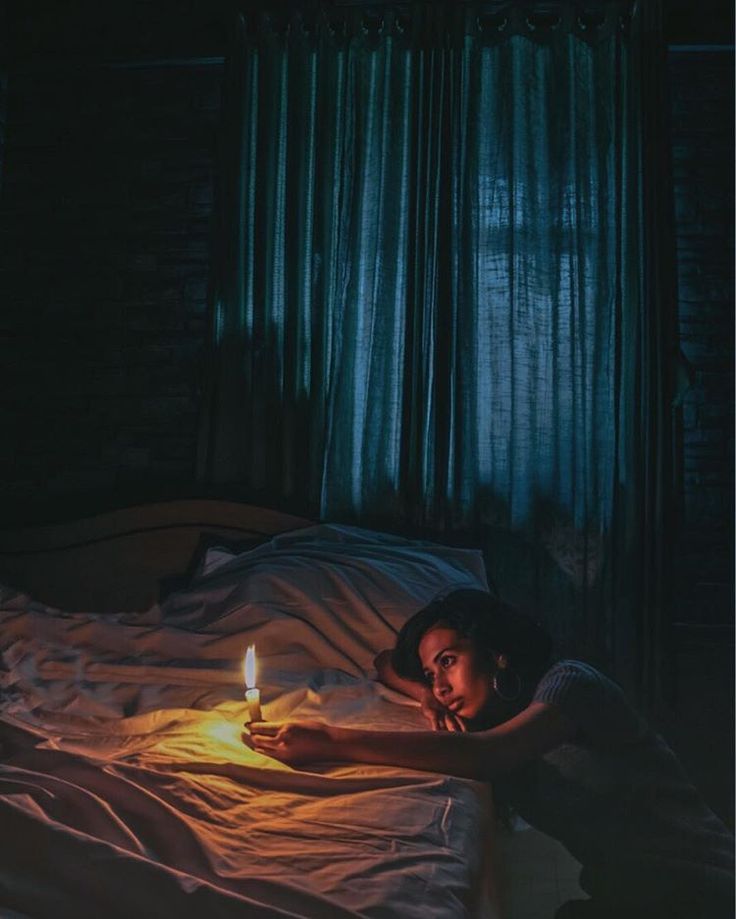 a woman laying in bed holding a lit candle