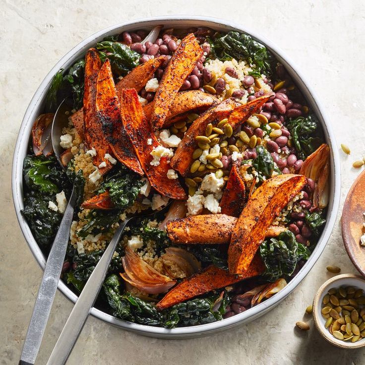 a bowl filled with lots of food next to two spoons and some nuts on the side