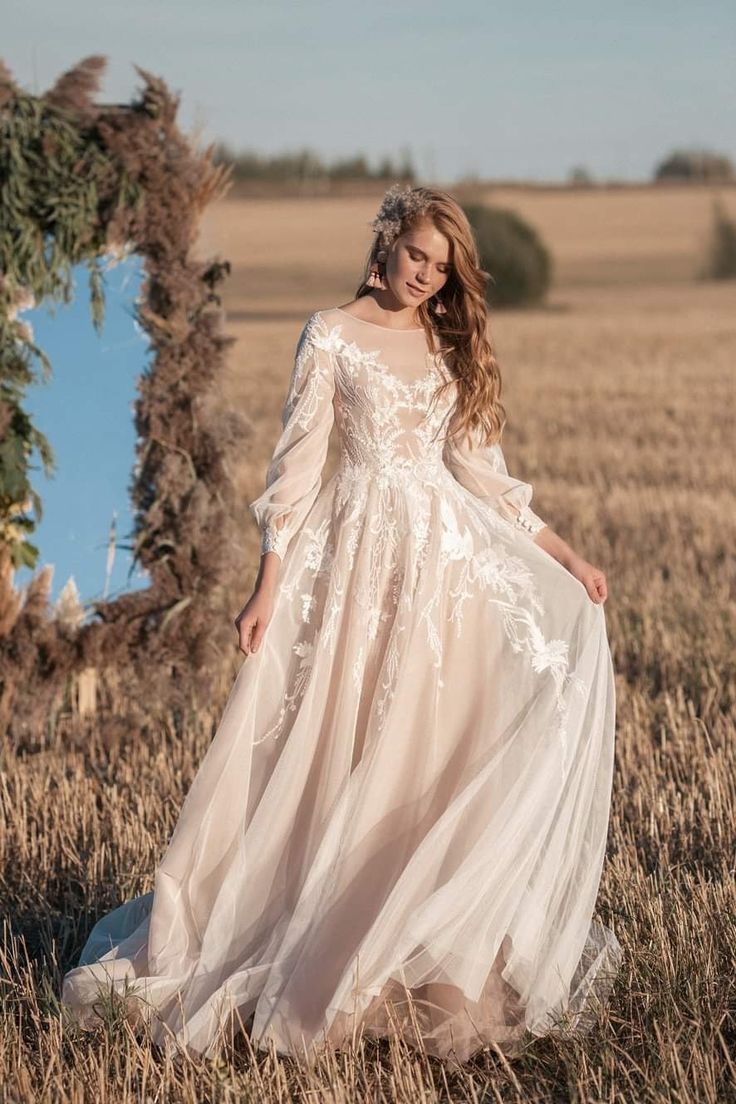 a woman standing in a field wearing a dress with long sleeves and an open back