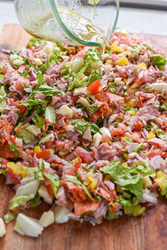 someone is pouring dressing onto a salad on a cutting board with lettuce and tomatoes