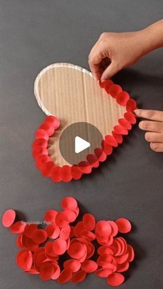 someone is making a heart out of paper and some red circles on the table with their hands