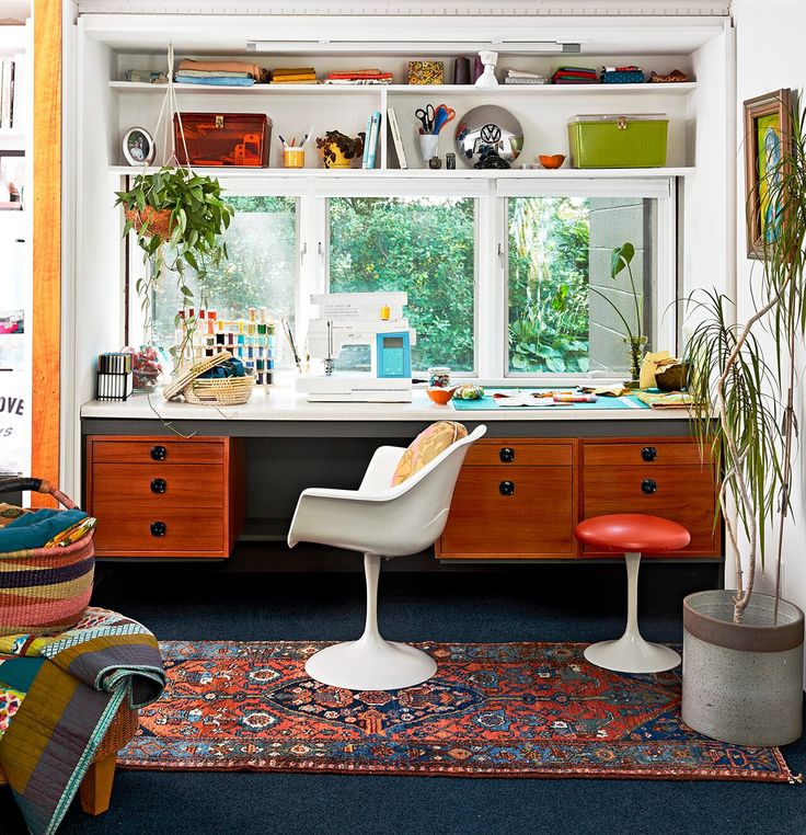 a room with a desk, chair and plants on the window sill in it