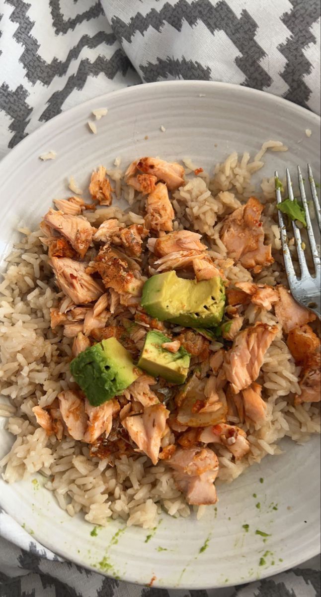 a white plate topped with rice and chicken next to a fork on a table cloth