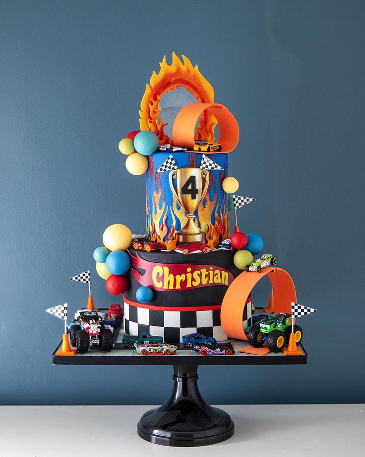 a three tiered cake with cars and balloons on the top is decorated like a fireman's helmet