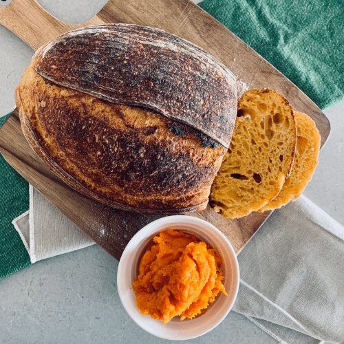 a loaf of bread sitting on top of a cutting board next to a bowl of butter