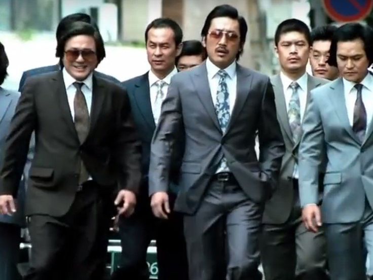 a group of men in suits and ties walking down the street with one man wearing sunglasses