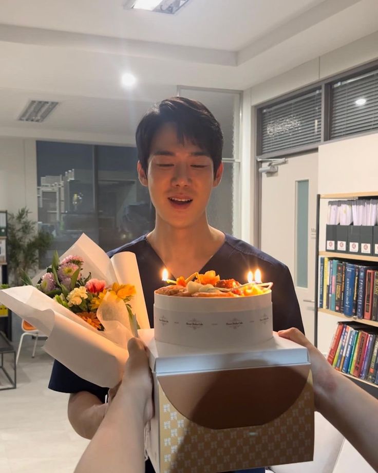 a young man holding a cake with candles on it and flowers in front of him