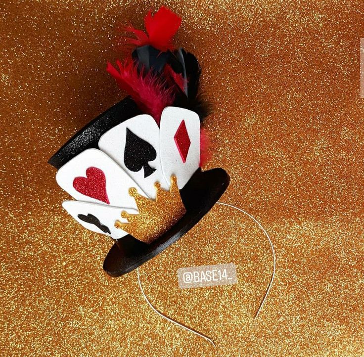 a black and white hat with playing cards on it's side sitting on a gold glitter surface