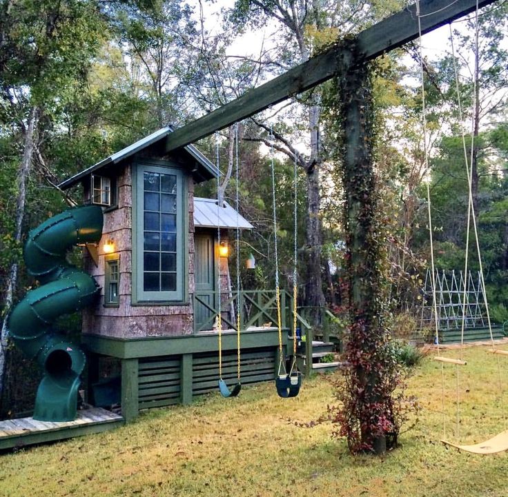 a small house with a green slide in the back yard and trees around it,