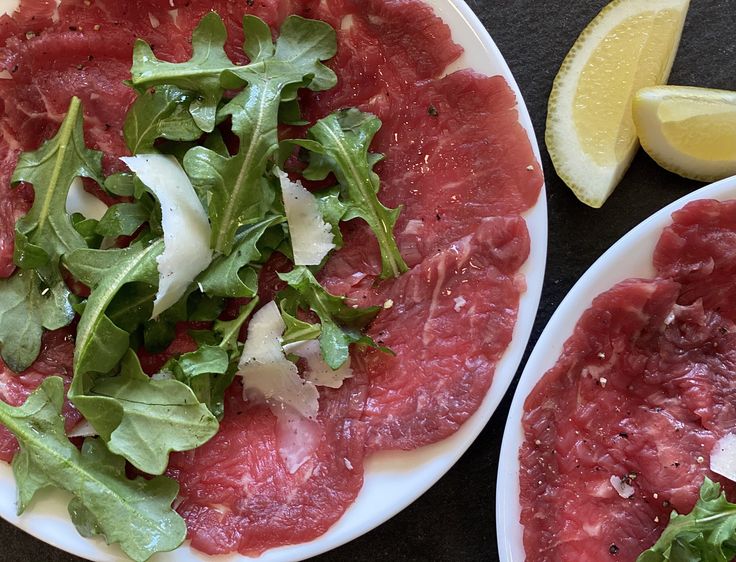 two white plates topped with meat and veggies next to sliced lemon wedges